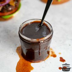 a jar filled with chocolate sauce sitting on top of a white counter next to two burgers