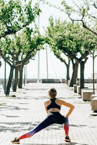 a woman is doing yoga outside on the sidewalk in front of some trees and benches