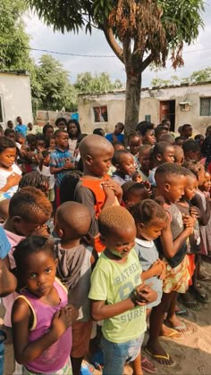 a group of children standing around each other in front of a tree and some buildings