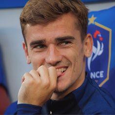 a close up of a person wearing a blue shirt and smiling at the camera with his hand on his chin