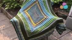 a crocheted blanket sitting on top of a metal chair next to a potted plant