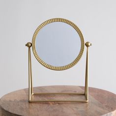 a round mirror sitting on top of a wooden table next to a small stand with a mirror