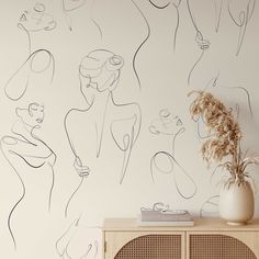 a white vase sitting on top of a wooden cabinet next to a wall covered in drawings