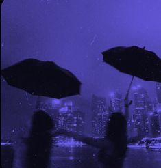 two people holding umbrellas in the rain with city lights and buildings in the background