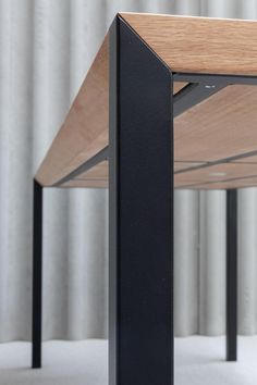 a wooden table with black metal legs and a white curtain in the backround