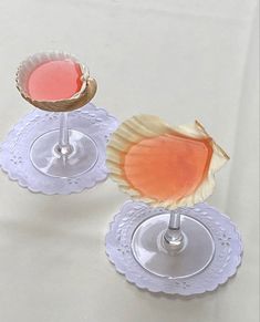 two wine glasses filled with pink liquid on top of white doily and silver rimmed saucers