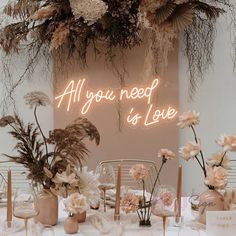 a table topped with lots of vases filled with flowers next to a neon sign that says will you marry me?