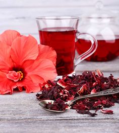 red tea with flowers and spoons on wooden table next to glass cups filled with liquid