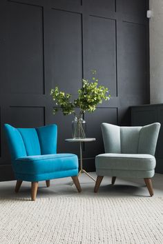 two blue chairs sitting next to each other in front of a black paneled wall