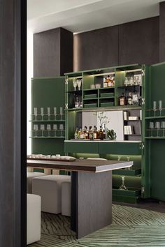 a green bar with lots of bottles and glasses on the shelves in front of it