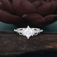 an engagement ring with a princess cut diamond set in the center on a piece of wood