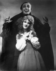 an old black and white photo of two people dressed as dracula and the woman is holding a doll in her arms