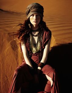 a woman sitting on top of a sandy dune in the desert wearing a headdress