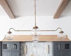 a kitchen with marble counter tops and blue cabinets, hanging lights over the sink area