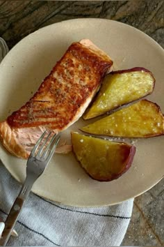 a white plate topped with fish and potatoes next to a fork on a tablecloth