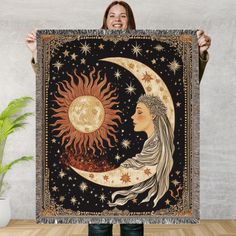 a woman holding up a tapestry with the sun and moon on it in front of her face