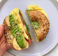 a sandwich with eggs, lettuce and tomato on a bagel bun is being held up by someone's hand