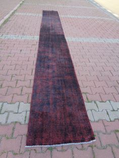 a red and black rug sitting on top of a brick road next to a sidewalk