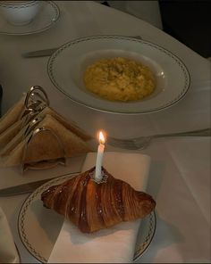 a candle is lit on top of a croissant at a table set for dinner