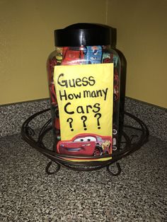 a glass jar filled with candy sitting on top of a counter next to a sign that says guess how many cars?