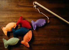 five different colored felt fish on a wooden table next to a knitting needle and thread