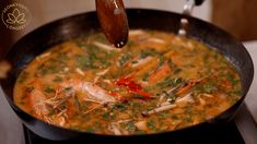 a skillet filled with soup on top of a stove next to a wooden spoon