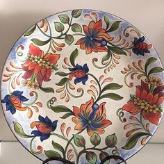 a decorative plate with flowers and leaves on it sitting on a shelf next to a pair of scissors