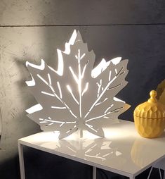 a white table topped with a yellow vase next to a cut out leaf shaped object