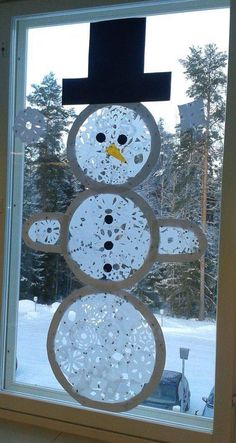 a snowman made out of paper sitting on top of a window sill in front of a snowy forest