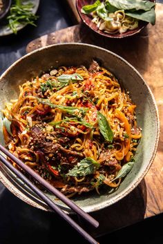 a bowl filled with noodles and meat on top of a wooden table next to chopsticks