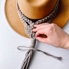 a person tying a hat on top of a white table with a gray rope around it