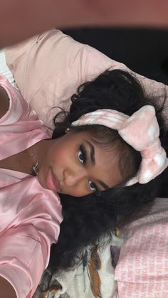 a woman laying on top of a bed wearing a pink shirt and bow tie headband