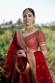 a woman in a red and gold lehenga is posing for the camera with her hand on her hip