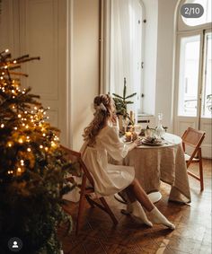 a woman sitting at a table in front of a christmas tree