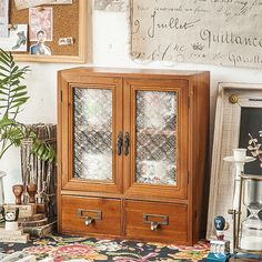 a wooden cabinet sitting on top of a rug next to a potted plant and framed pictures