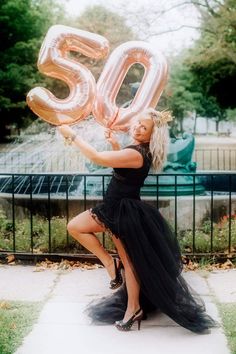 a woman in a black dress is holding up some large balloons that spell the number 50