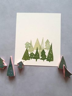 three christmas trees are next to a white card with green and gold foil on it