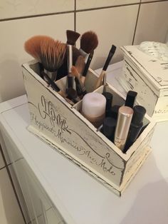 a wooden box filled with lots of different types of makeup brushes and other items on top of a counter