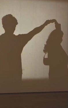 two people standing in front of a wall with their shadow on the wall and one person holding his hand up