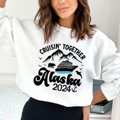 a woman wearing a white sweatshirt that says cruising together alaska in front of a mountain range