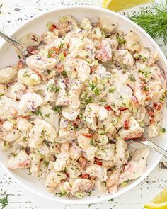 a white bowl filled with chicken salad next to lemon wedges and dill sprigs