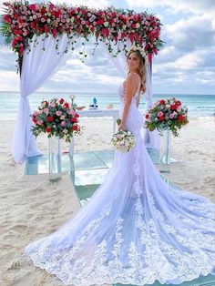 a woman in a wedding dress standing on the beach under an arch decorated with flowers