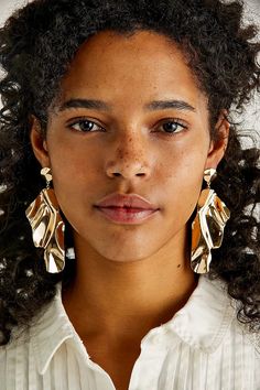 a close up of a person wearing large gold earring's and a white shirt