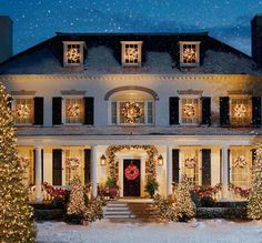 a large white house with christmas lights on it's windows and wreaths around the front door