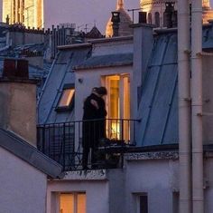 two people standing on top of a roof next to tall buildings with towers in the background