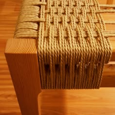 a close up of a wooden bench with rope on the seat and wood flooring