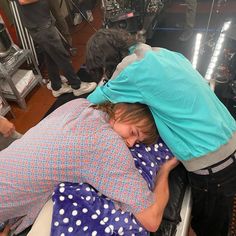 a woman laying on top of a bed in a room with other people standing around