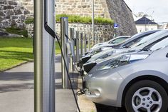 several electric cars are parked on the side of the road in front of a stone wall