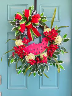 a watermelon wreath on a blue door with red and white flowers, greenery and ribbon