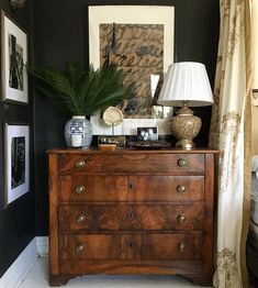 a wooden dresser sitting in front of a window next to a lamp and pictures on the wall